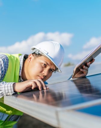 Young Asian Inspector Engineer man working at solar farm, Technician or supervisor male in white helmet Checking operation of sun and photovoltaic solar panel in station, copy space